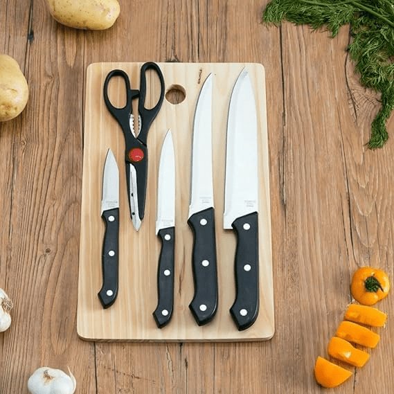 Sharp kitchen knives and scissors on a wooden cutting board with vegetables around, suitable for home cooking and food preparation.